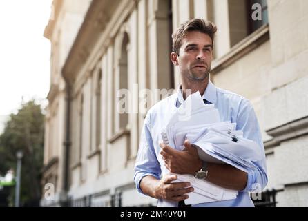 J'ai beaucoup de travail à faire. un jeune homme stressé tenant un tas de documents en papier tout en marchant au travail le matin. Banque D'Images