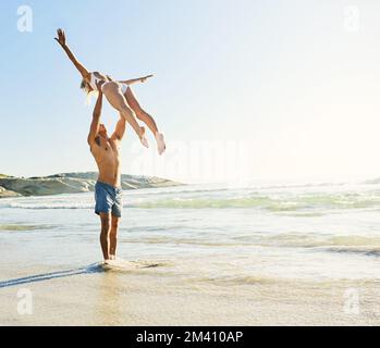 Apportez les jours de plage. un jeune homme qui lève sa petite amie dans les airs à la plage. Banque D'Images