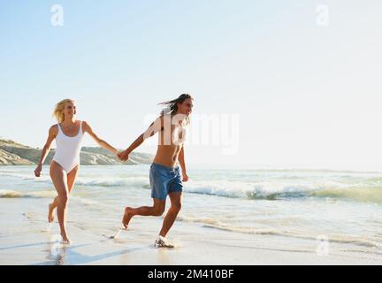 Courir avec la brise de l'océan. un jeune couple qui court le long de la plage. Banque D'Images
