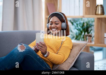 La maison est mon endroit heureux. une jeune femme attrayante portant un casque tout en utilisant son téléphone portable. Banque D'Images
