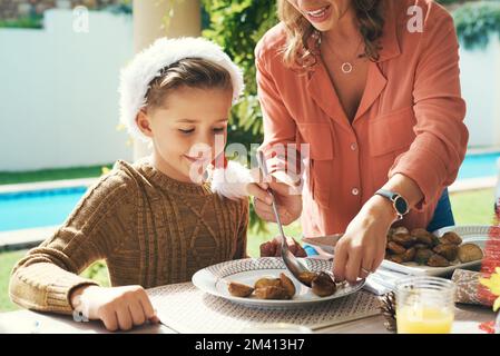 Il a hâte d'y aller. Une mère qui sert de la nourriture pour son petit garçon lors de la fête du déjeuner de Noël. Banque D'Images