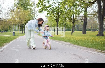 Vélo, apprendre et la mère enseignant fille sur la route à l'extérieur, ayant le plaisir et le collage. Soins, éducation et maman heureuse montrant à l'enfant comment monter à vélo Banque D'Images