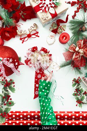 Les femmes font main la décoration de Noël rouge sur fond blanc avec des branches de sapin vert, boîte-cadeau, rubans et fleurs de Poinsettia. Vue de dessus Banque D'Images