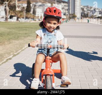 Portrait, petite fille et vélo sur le trottoir, apprendre à faire du vélo ou un développement sain de l'enfance. Joyeux enfant à faire du tricycle avec casque, sécurité Banque D'Images