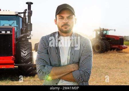 Un agriculteur barbu se trouve devant un tracteur agricole Banque D'Images