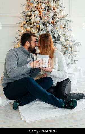 couple heureux près des boîtes-cadeaux et de l'arbre de noël. couple embrassant et regardant l'un l'autre près de l'arbre de noël. Banque D'Images