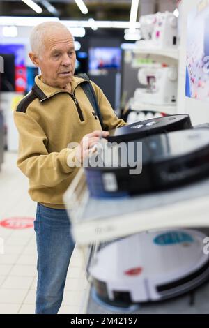 homme âgé qui choisit un robot-aspirateur dans la salle d'exposition du magasin d'appareils électriques Banque D'Images