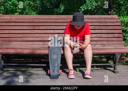 Garçon avec un skateboard en plastique assis sur la paillasse et fixe au téléphone. Banque D'Images