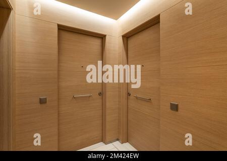 La lumière douce de la niche sous le plafond illumine les portes et les murs dans le couloir commun. L'intérieur est fait dans le même style de bois précieux. Portes d'entrée Banque D'Images