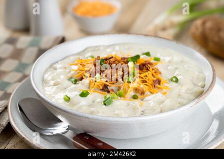 Soupe crémeuse de pommes de terre avec morceaux de bacon, fromage cheddar râpé et oignons verts hachés dans un bol blanc Banque D'Images
