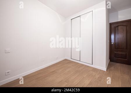 Cette chambre dispose d''une armoire intégrée personnalisée dotée de portes coulissantes blanches, de murs blancs lisses peints en blanc et de portes en bois sombre Banque D'Images