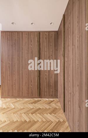 Une armoire avec des portes-racines en bois dressing L deux murs d'une pièce avec lampes intégrées au plafond et parquet en chêne français à chevrons Banque D'Images