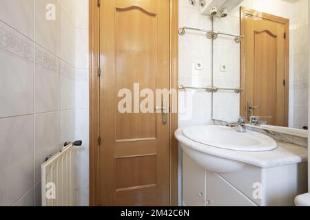 Une petite salle de bains avec un radiateur en aluminium, un meuble de salle de bains blanc avec un miroir et un comptoir en marbre et des barres pour contenir des serviettes Banque D'Images