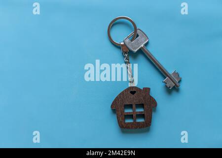 Clé avec porte-clés maison sur fond bleu coloré. Agent immobilier. Acheter une maison, un appartement. Banque D'Images