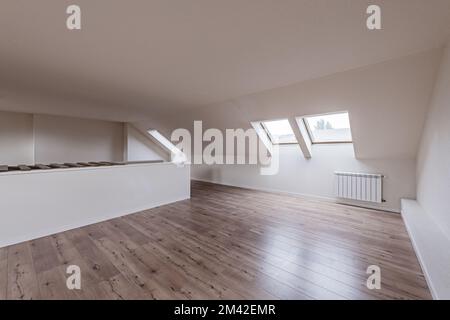 Grenier d'une maison unifamiliale vide avec des puits de lumière sur les avant-toits du toit avec plancher flottant en châtaignier Banque D'Images