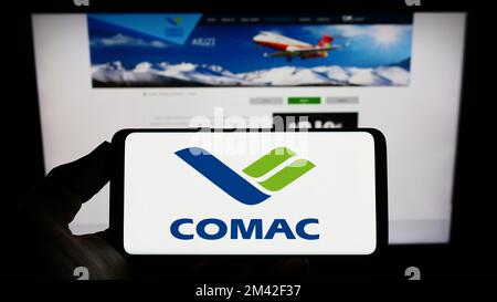 Personne tenant un smartphone avec le logo de commercial Aircraft Corporation of China (COMAC) à l'écran devant le site Web. Mise au point sur l'affichage du téléphone. Banque D'Images