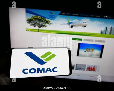 Personne tenant un téléphone portable avec le logo de commercial Aircraft Corporation of China (COMAC) à l'écran devant la page Web. Mise au point sur l'affichage du téléphone. Banque D'Images