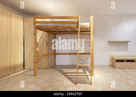 Cette chambre est dotée d''une structure en pin avec une échelle et un sommier pour un lit surélevé, de sols en grès clair et d''un mur bordé de meubles en bois Banque D'Images