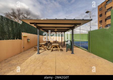 Une pergola couvrant des bancs en bois à côté d'un court de tennis dans un immeuble résidentiel Banque D'Images