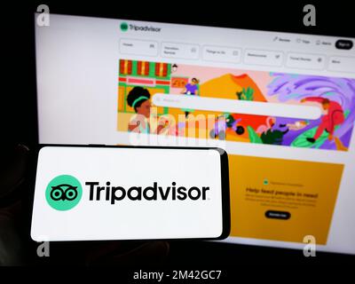 Personne tenant un smartphone avec le logo de la compagnie de voyage américaine Tripadvisor Inc. À l'écran devant le site Web. Mise au point sur l'affichage du téléphone. Banque D'Images