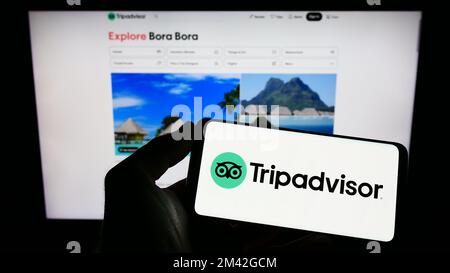 Personne tenant un téléphone mobile avec le logo de la compagnie américaine de voyage Tripadvisor Inc. À l'écran en face de la page Web d'affaires. Mise au point sur l'affichage du téléphone. Banque D'Images