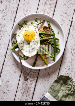 Une assiette de saumon rôti recouverte d'asperges cuites à la vapeur et d'un œuf frit. Banque D'Images