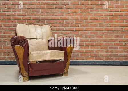 Un vieux fauteuil avec des traces de temps contre un mur de briques. Banque D'Images