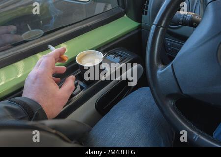 Fumer en conduisant une voiture. Cigarette à la main. Tasses à café jetables en papier Banque D'Images