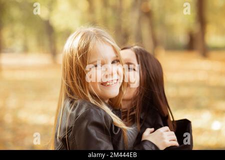 Mignonne, heureuse, joyeuse famille de la jeune mère et petite fille embrassant et embrassant, regardant l'appareil photo dans le parc d'automne Banque D'Images