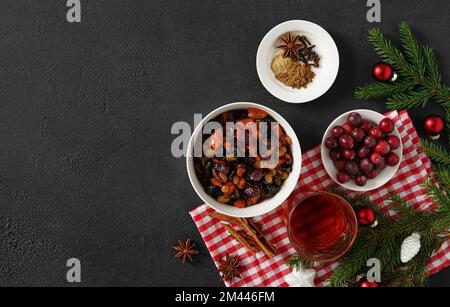 Ingrédients pour gâteau de fruits de Noël sur fond sombre, noix et fruits secs trempant l'eau-de-vie ajoutée dans le bol en céramique. Vue de dessus. copier l'espace Banque D'Images