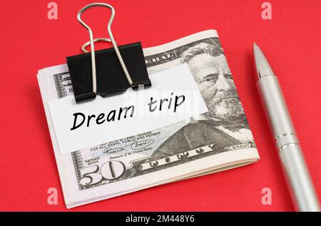 Concept financier et commercial. Sur fond rouge se trouve un stylo et des dollars fixés avec un clip avec l'inscription sur papier - Voyage de rêve Banque D'Images