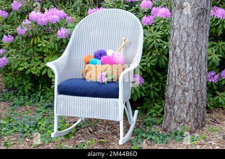 Fil coloré dans un panier sur un fauteuil à bascule en osier blanc dans un jardin de rhododendron Banque D'Images