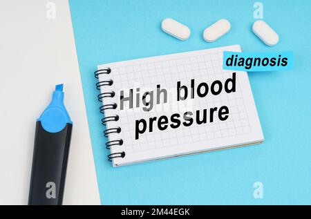 Médecine et concept de santé. Sur une surface blanche et bleue se trouvent des pilules, un marqueur et un carnet avec l'inscription - hypertension, un autocollant avec Banque D'Images