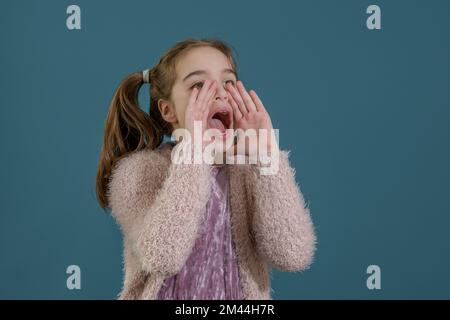 Appelez l'attention. Portrait d'une jeune fille dans un chandail rose à bouche ouverte et de grands yeux isolés sur fond bleu Banque D'Images