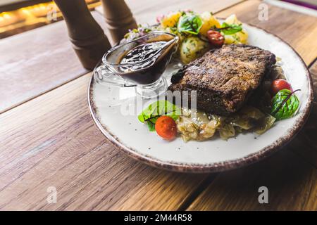 Assiette blanche avec côtes de porc croustillantes sur le chou braisé, sauce foncée et pommes de terre bouillies. Gros plan portrait. Prise de vue en intérieur. Photo de haute qualité Banque D'Images