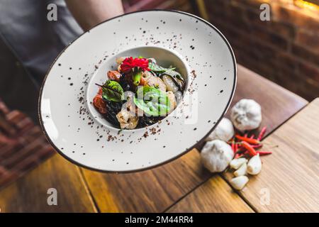 Un serveur méconnu servant des crevettes. Pâtes à base de tagliolini noires aux crevettes et aux herbes. Intérieur du restaurant. Photo de haute qualité Banque D'Images