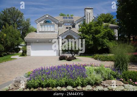 Maison contemporaine de style cottage en briques grises avec cour avant paysagée en été. Banque D'Images