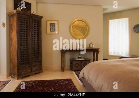 Vieille table en bois et armoire dans le style marocain décoré chambre principale avec plaque de métal décoratif doré sur le mur à l'intérieur de la maison contemporaine. Banque D'Images