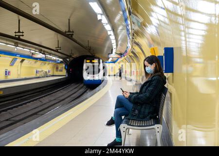 Jeune femme latine assise et portant un masque chirurgical avec un smartphone en attendant dans le métro ou la gare Banque D'Images