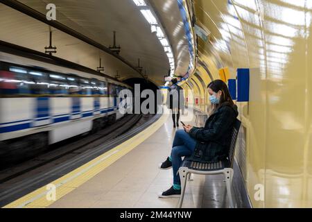 Jeune femme latine assise et portant un masque chirurgical avec un smartphone en attendant dans le métro ou la gare Banque D'Images