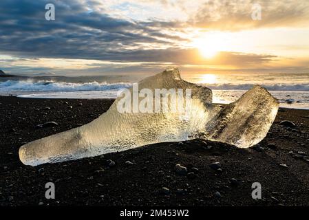 Iceberg rétro-éclairé sur le sable noir de Breiðamerkursandur ou Diamond Beach au crépuscule, en Islande, à côté de la lagune du glacier Jökulsárlón Banque D'Images