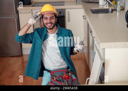 Un ouvrier professionnel souriant en uniforme assemble des meubles sur la cuisine. Concept de réparation Banque D'Images