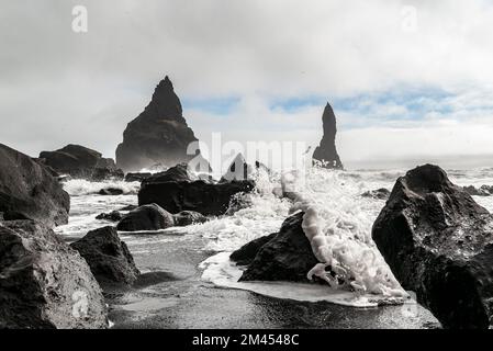 Les vagues s'écrasant contre les rochers noirs de basalte de la plage de Reynisfjara, avec les piles de la mer de Reynisdrangar en arrière-plan, près de Vík í Mýrdal, en Islande Banque D'Images