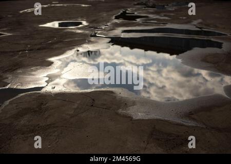 Grande flaque sur asphalte. Flaques de sol après la pluie. Précipitations en ville. Réflexion des nuages dans l'eau. Banque D'Images