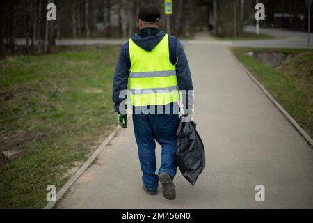 L'employé collecte les déchets. L'homme porte le paquet. Sac noir dans sa main. Concierge sur la route. Banque D'Images