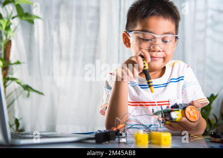 Enfant asiatique assemblant le projet de travail de robot de voiture Arduino à la maison Banque D'Images