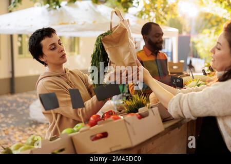 Personne joyeuse prenant un sac de légumes biologiques pour livrer la commande de nourriture bio sur vélo, parlant à la femme vendeur au marché local. Un préposé à la livraison de produits alimentaires s'est chargé de ramasser des produits écologiques frais dans un sac à dos. Banque D'Images