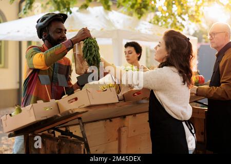 Jeune vendeur local donnant commande de bio-produits naturels à livreyman, en aidant avec les fruits et légumes livraison de nourriture. Femme agriculteur préparant des produits écologiques biologiques sur le marché des agriculteurs. Banque D'Images