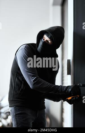 Soyez toujours à l'affût. un criminel masqué s'occupe de la serrure d'une porte dans un garage. Banque D'Images