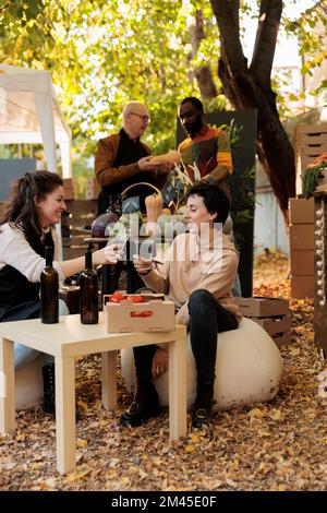 Les femmes souriantes se régent de verres de vin biologique au salon de la gastronomie, goûtant des produits faits maison et des boissons à l'extérieur. Les jeunes apprécient une bouteille de vin naturel frais et goûtant des produits sains. Banque D'Images